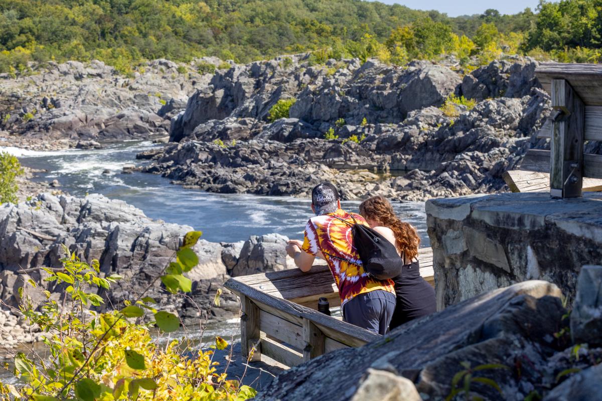 Man in Tie Dye and a Woman in Black Overlooking the Water at Great Falls Park