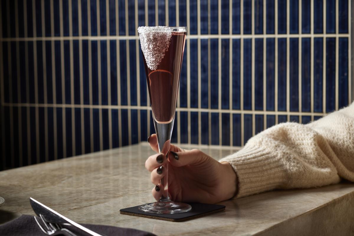 Woman's hand holding the stem of a champagne flute with a cranberry-colored cocktail