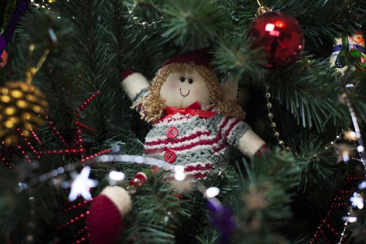 A cloth doll in a festive sweater sitting in a Christmas tree.