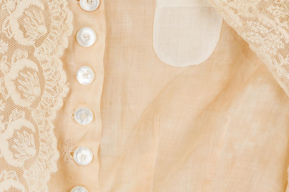 A close-up of an old garment with white buttons and cream-colored lace.