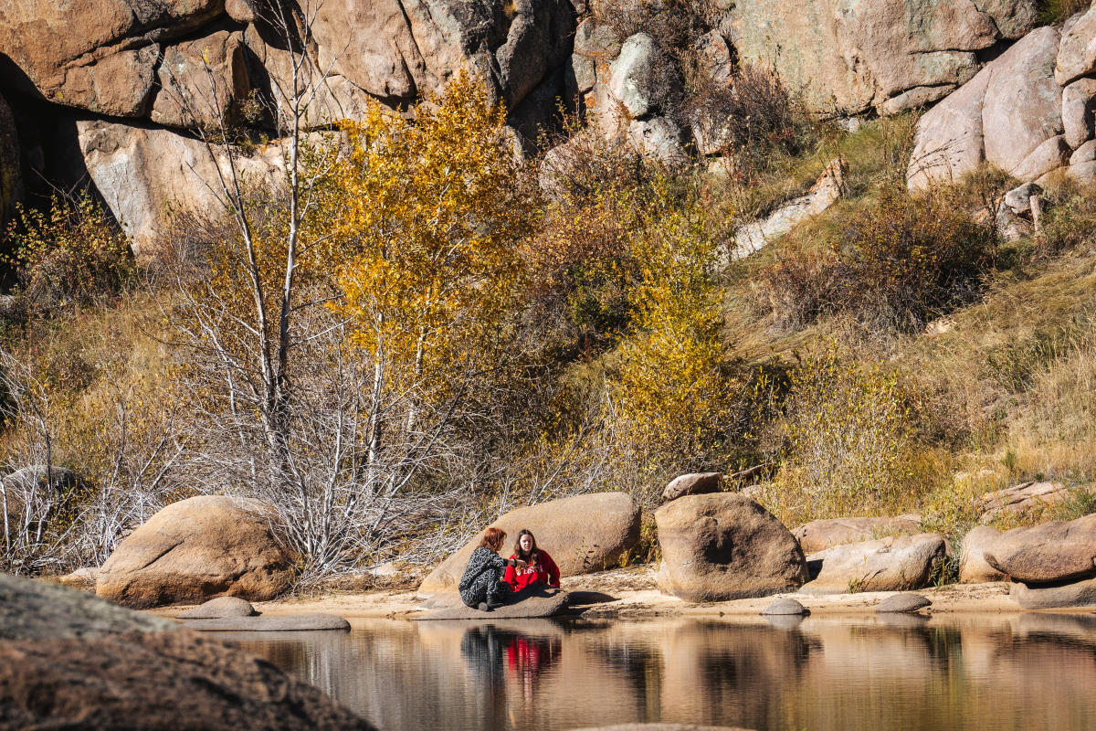 Two people sitting at the shore of a lake.