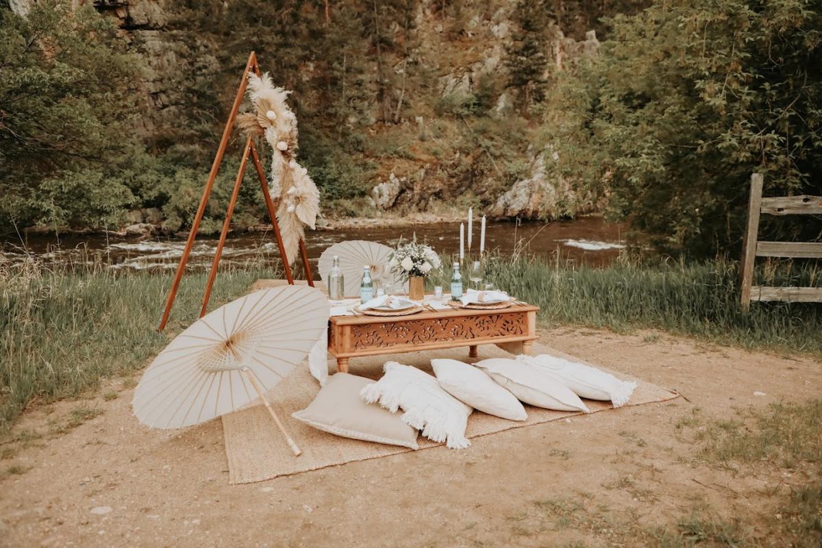 A small, low table next to a river with pillows for chairs and an artsy umbrella to the side