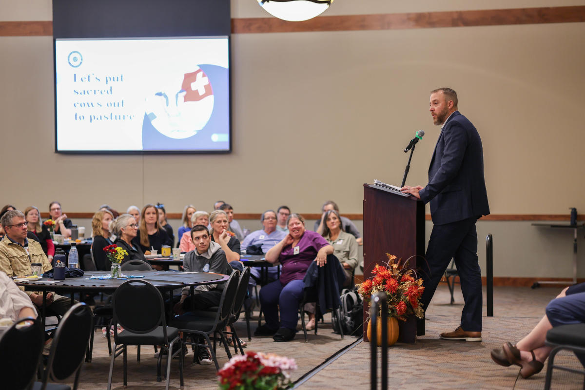 A man standing on a stage at a podium speaking to a group of people