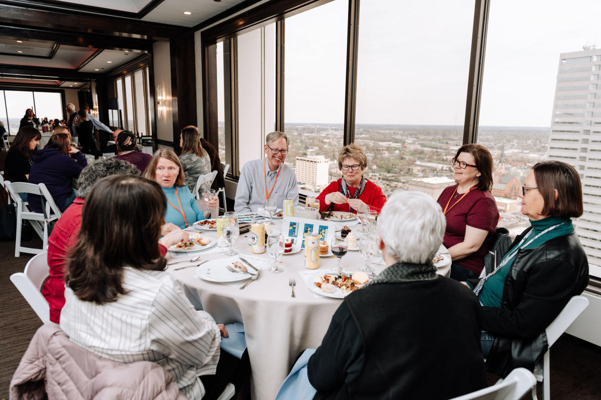 Group eating at a round table with a skyline view of Fort Wayne out the window behind them
