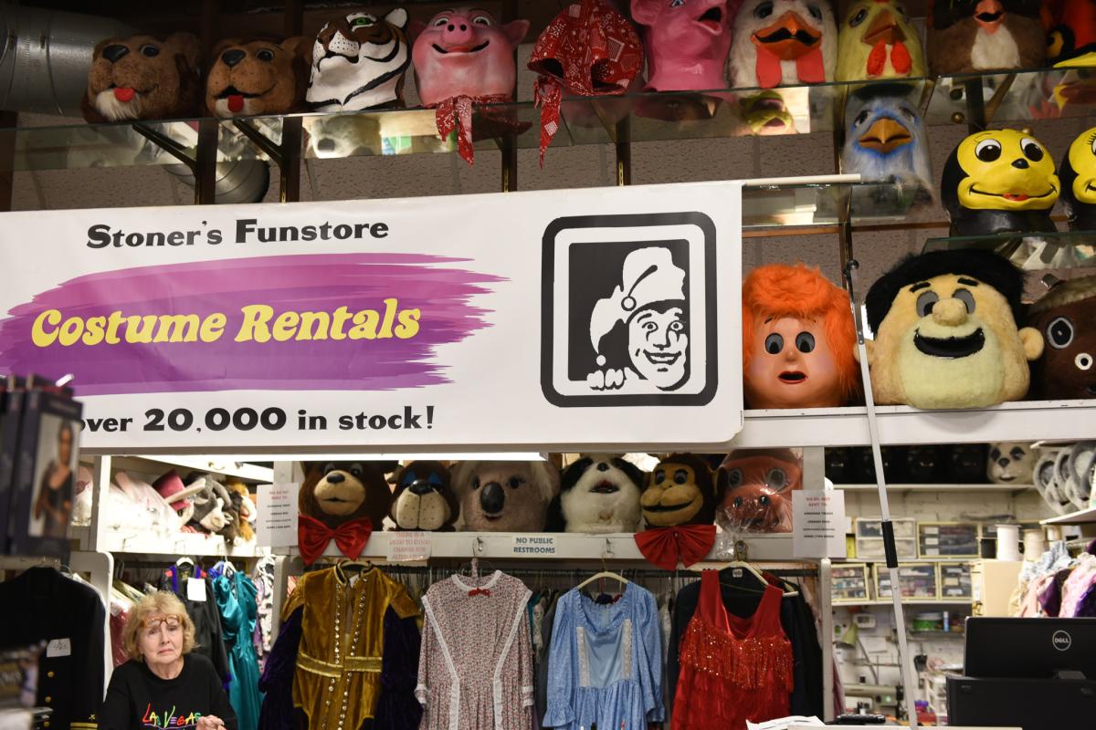 The words "Costume Rental" written on large sign surrounded by masks. A woman is in the bottom left hand corner of the picture