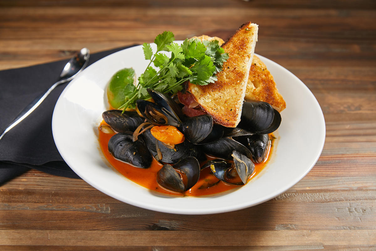 Plate with mussels, toast, and cilantro with an orange sauce