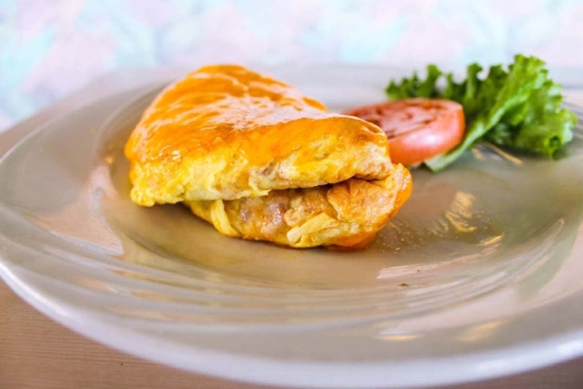 a close-up picture of an omelet garnished with lettuce and tomato on a white plate