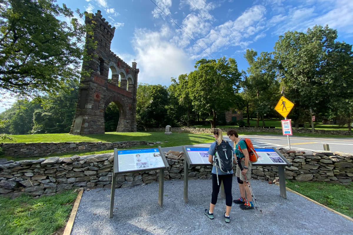 Two people reading an informational plate in front of the War Correspondents Arch 