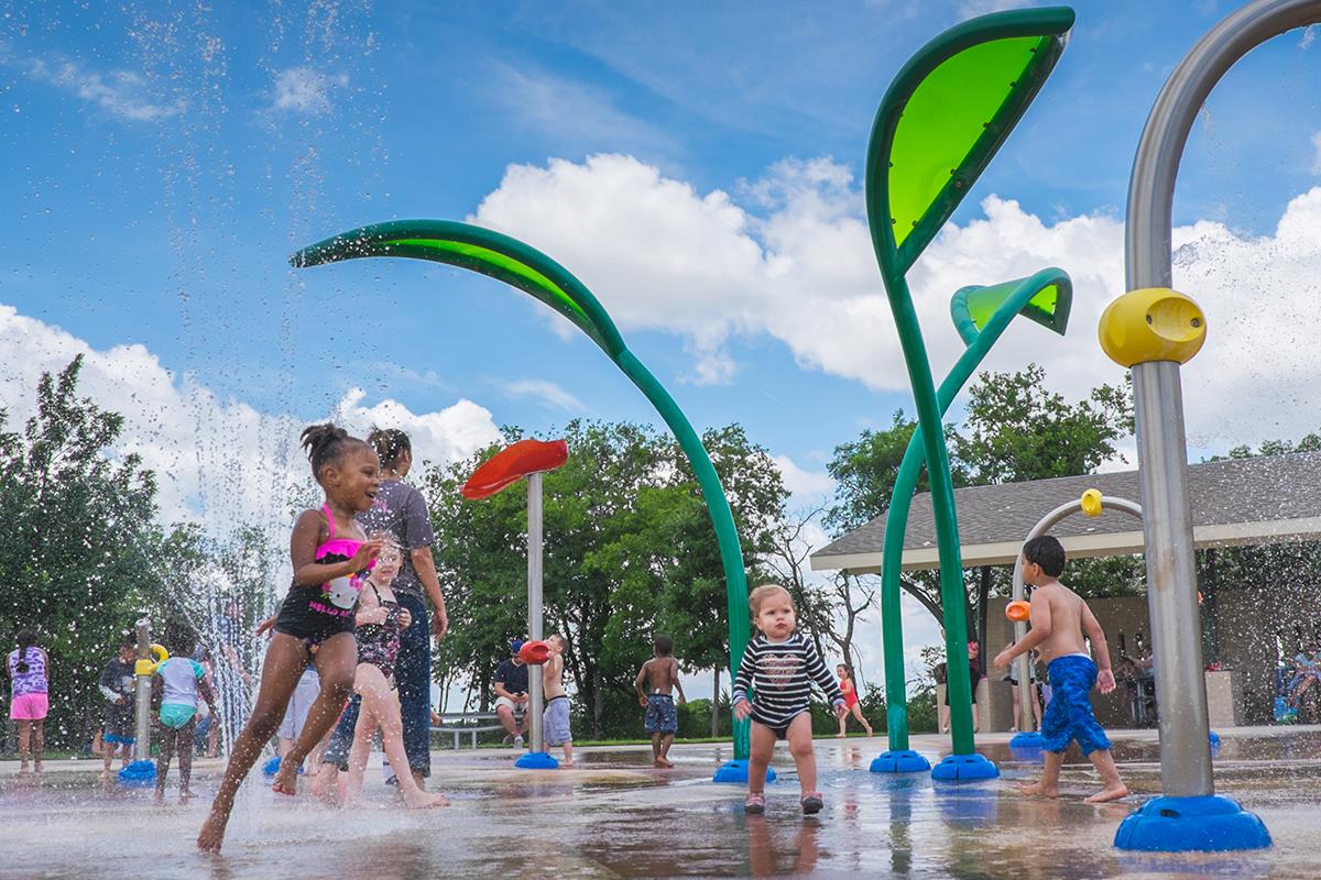 Children running around as water sprays around them on a splash pad