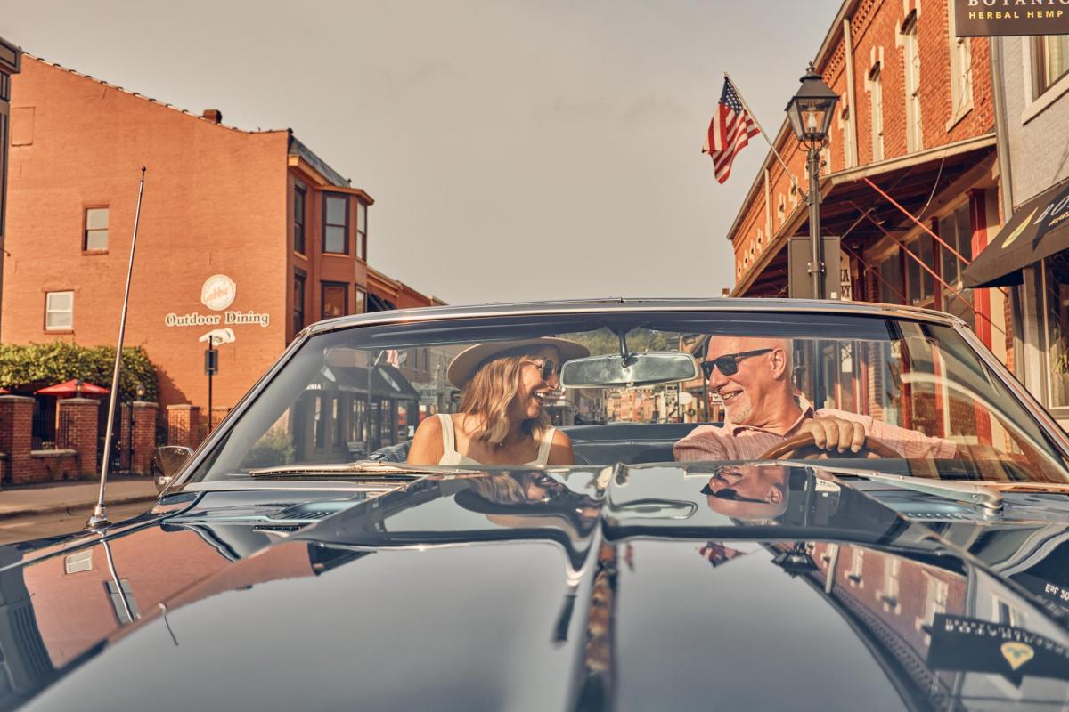 A couple sitting in a convertible car, driving down Main Street Galena.