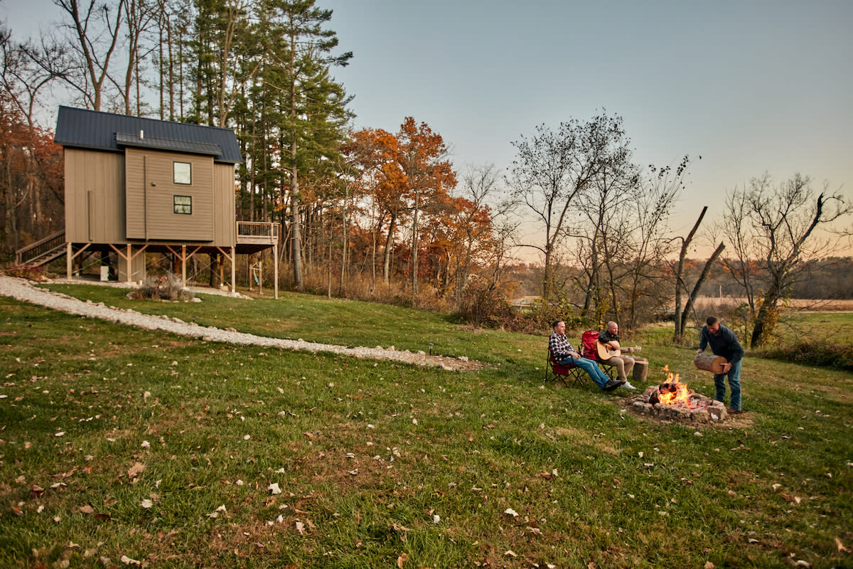 Group of people around a bonfire at a cabin in the woods