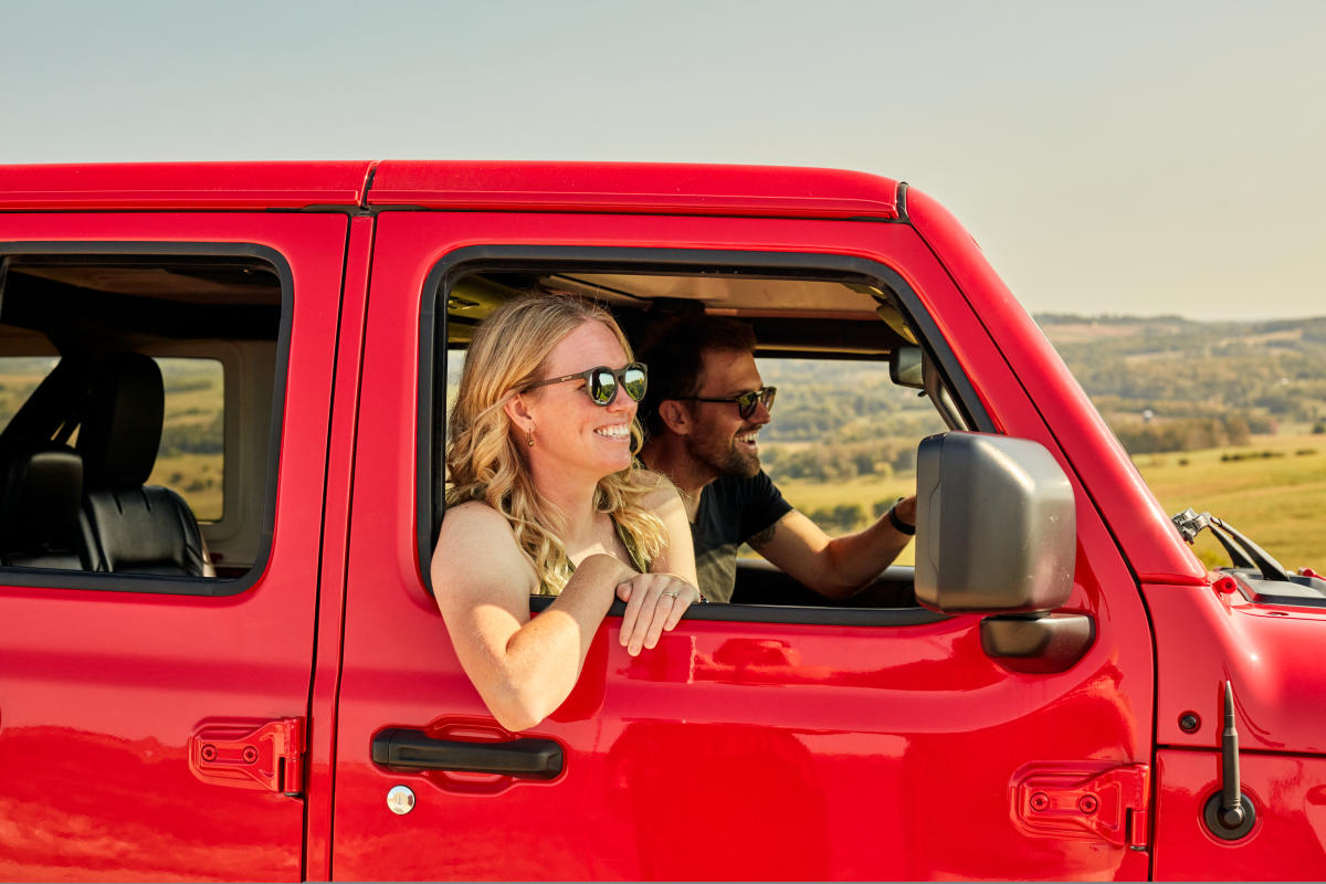Two people riding in a red vehicle at a scenic overlook. Both smiling, looking out the front of the vehicle.