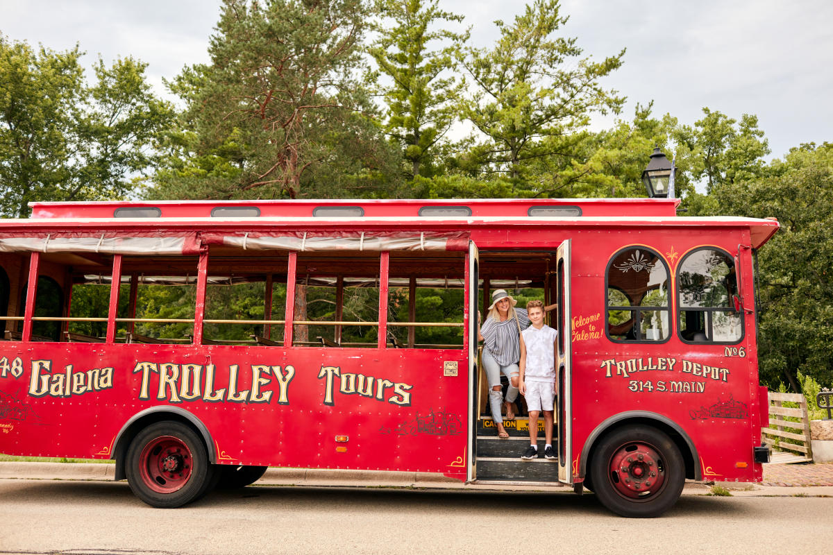 A woman and child standing in front of a red trolley bus.