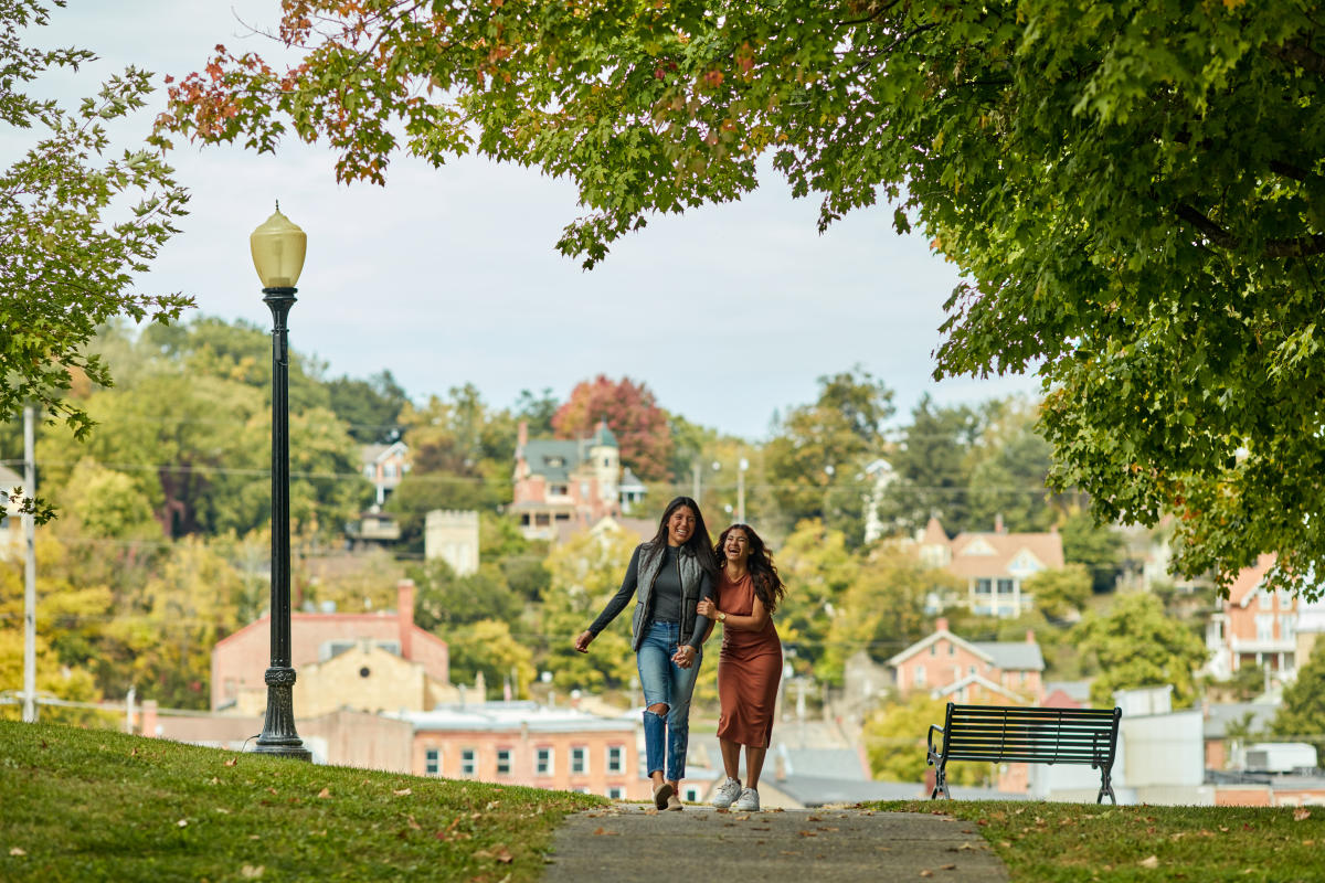 Two people laughing and walking in Grant Park, in the Fall. Behind them is the view of downtown Galena.