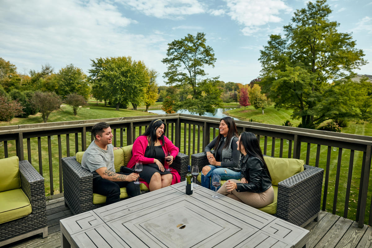 Four people sitting on a deck at the Wyndham Garden Hotel, having a conversation. The season is late summer with some color on the leaves.