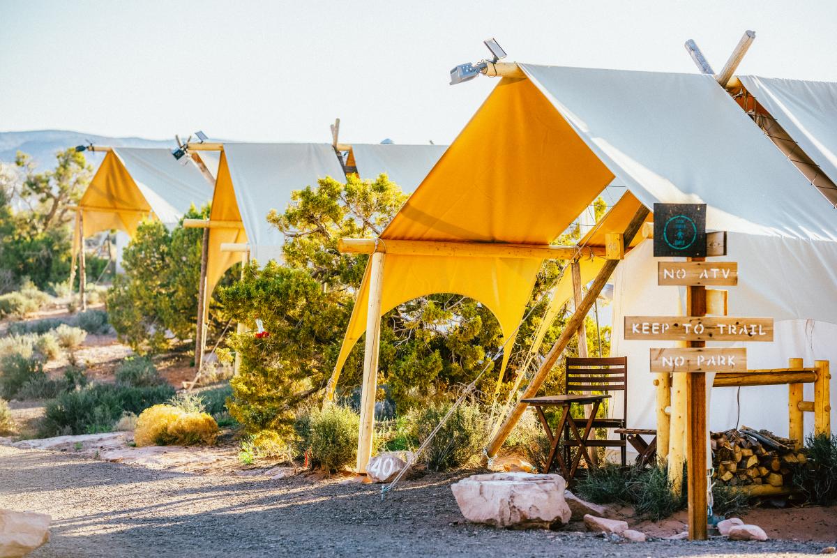 Safari-style canvas tents at Under Canvas Moab surrounded by desert vegetation under a bright blue sky.
