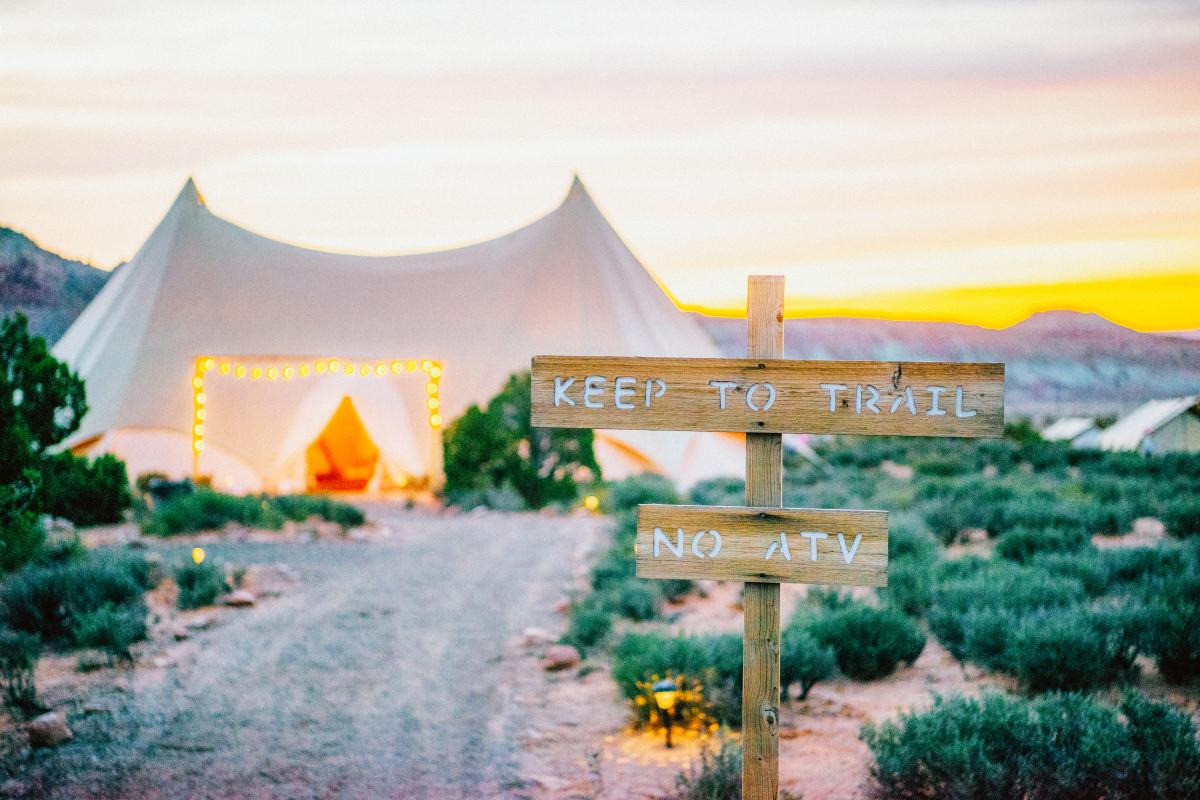 Glamping tents at sunset with string lights and a wooden trail sign at Under Canvas Moab.