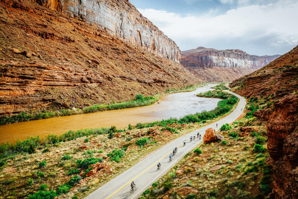 An aerial view of a scenic cycling and running route located along Utah State Route 128 (the Upper Colorado River Scenic Byway) just outside of Moab, Utah, hugging the winding red rock gorges of the Colorado River.