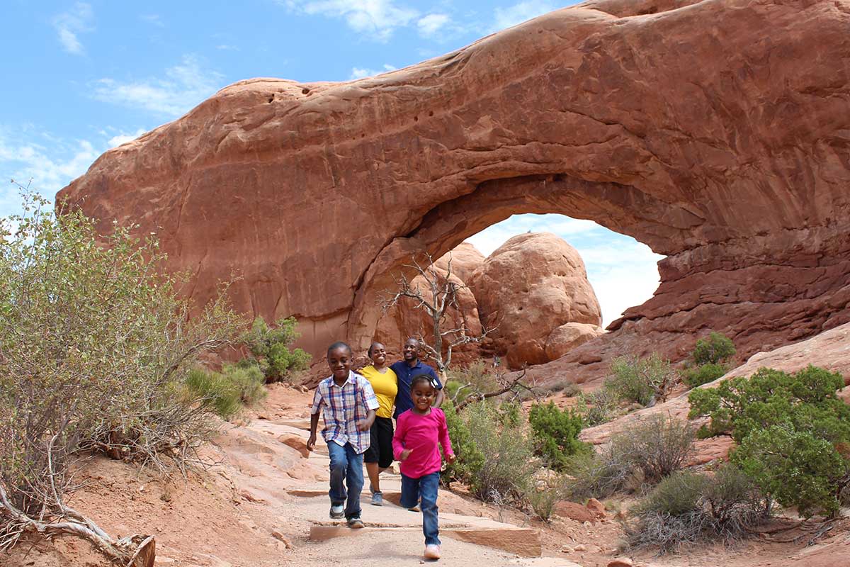 A family of four hikes amongst sandstone arches at the Windows Section in Arches National Park.