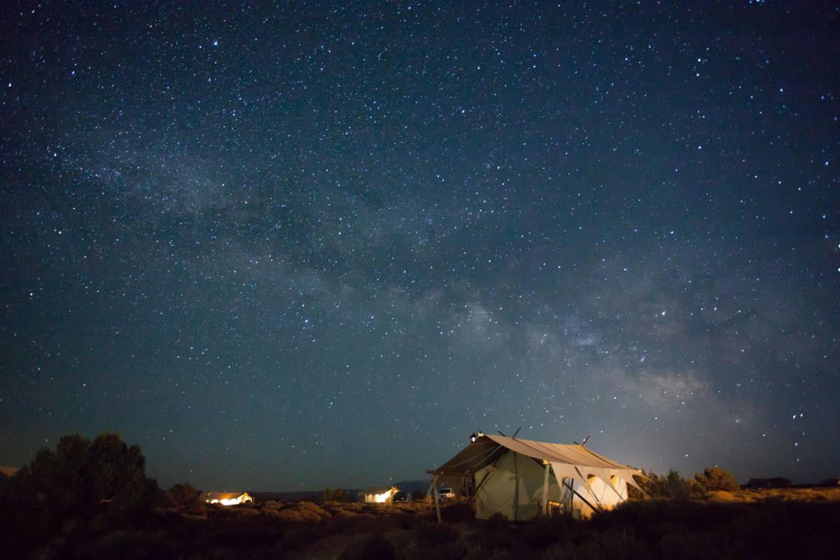 A safari-style canvas tent at Under Canvas Moab at night, under a star-filled sky.