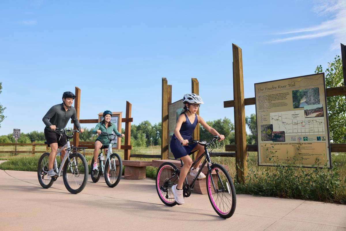 Family Biking outdoors on the Poudre River Trail with sign behind them