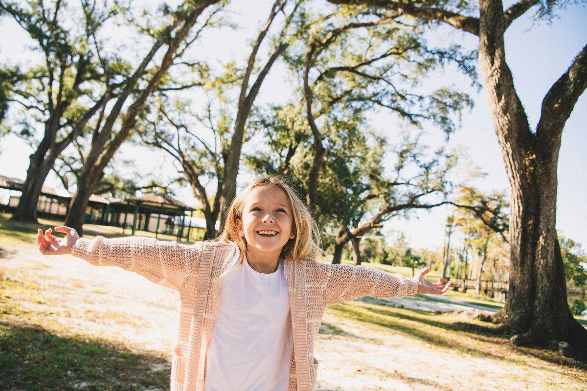 A young girl spreads out her arms and spins beneath the oaks in a local Park