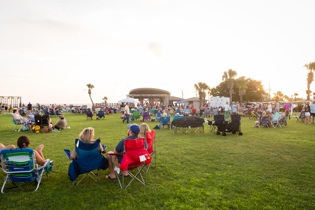 A group of people in lawn chairs listen to live music at a celebration in a local park