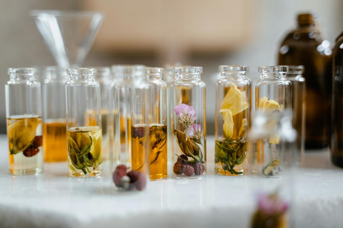 Glass vials filled with herbs, flowers and botanical tinctures on a white table.
