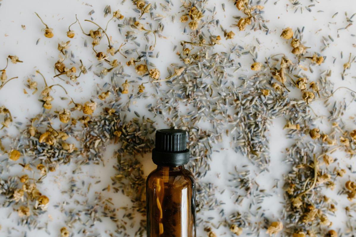 Amber glass bottle surrounded by scattered dried chamomile and lavender on a white surface.