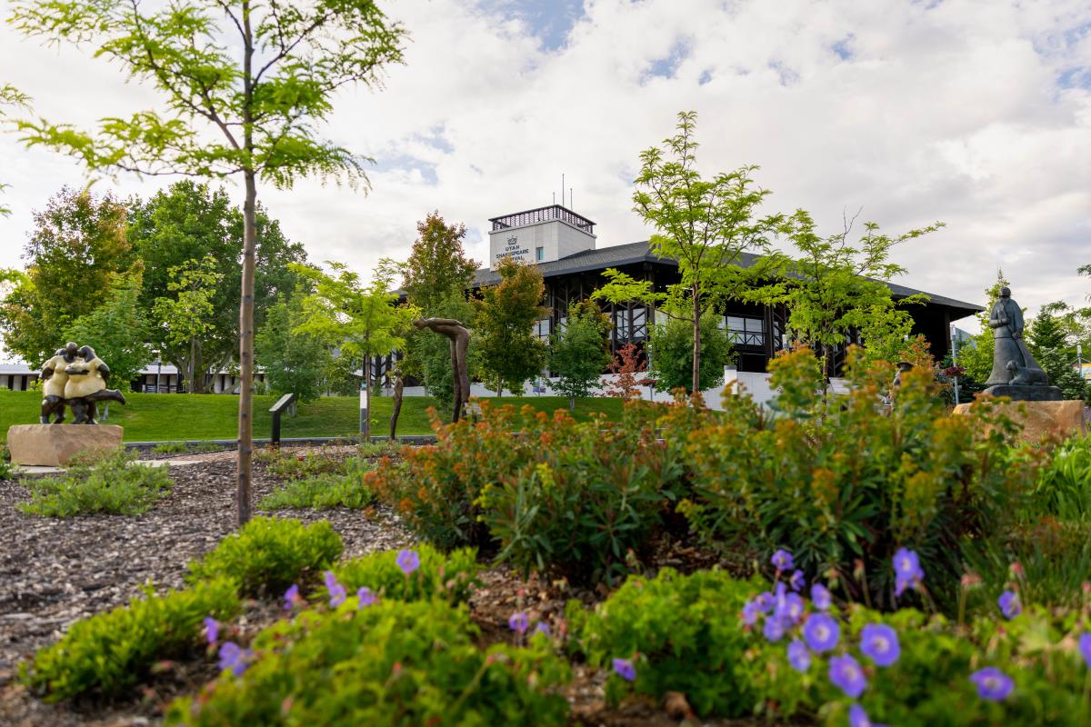 Blooming flower gardens with modern sculptures and a large theater in the background.