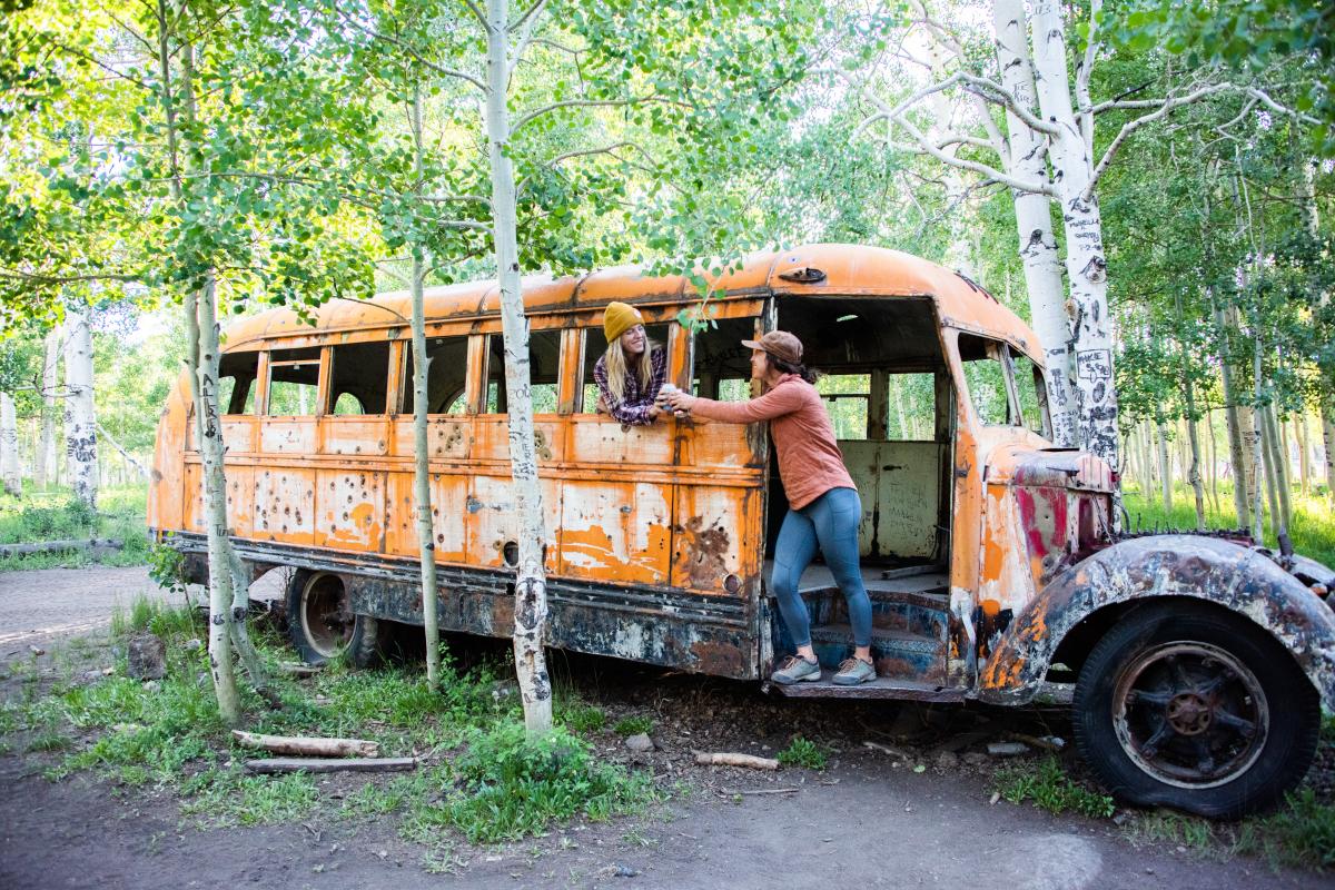 Two women standing in an abandoned yellow bus among bright green aspens near Brian Head Utah.