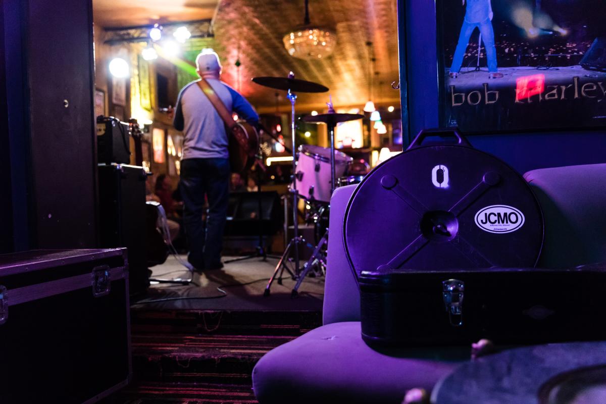 guitar case in front of drum set and guitar player on stage