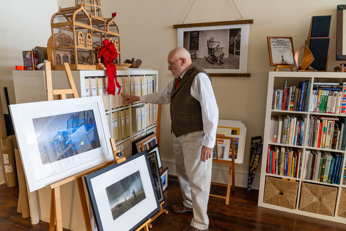 a man in his studio points at an archival box sitting with others on bookshelf