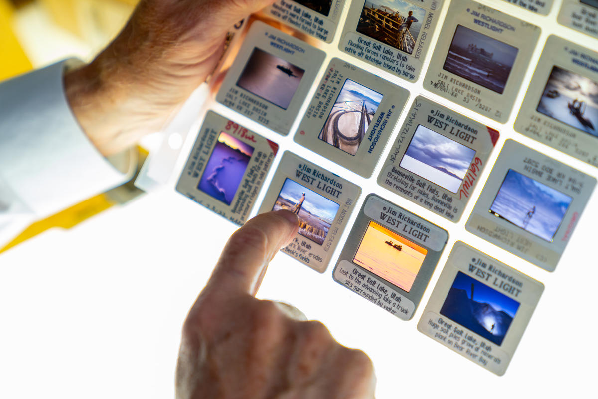 a hand points at image slides in a clear sheet, a light table is in the background