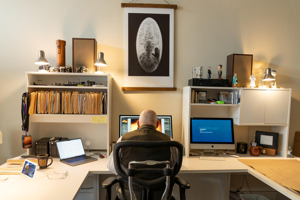 man sits at a desk in an office, with his back to the camera