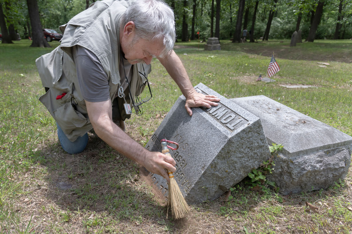 man kneeling brushing off broken headstone