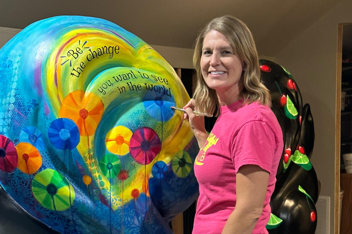 woman wearing a pink shirt paints a colorful mural