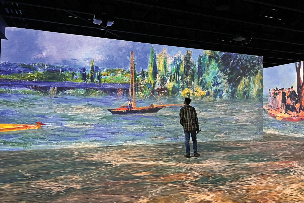a man stands looking at a wall with a digital painting projected on it.