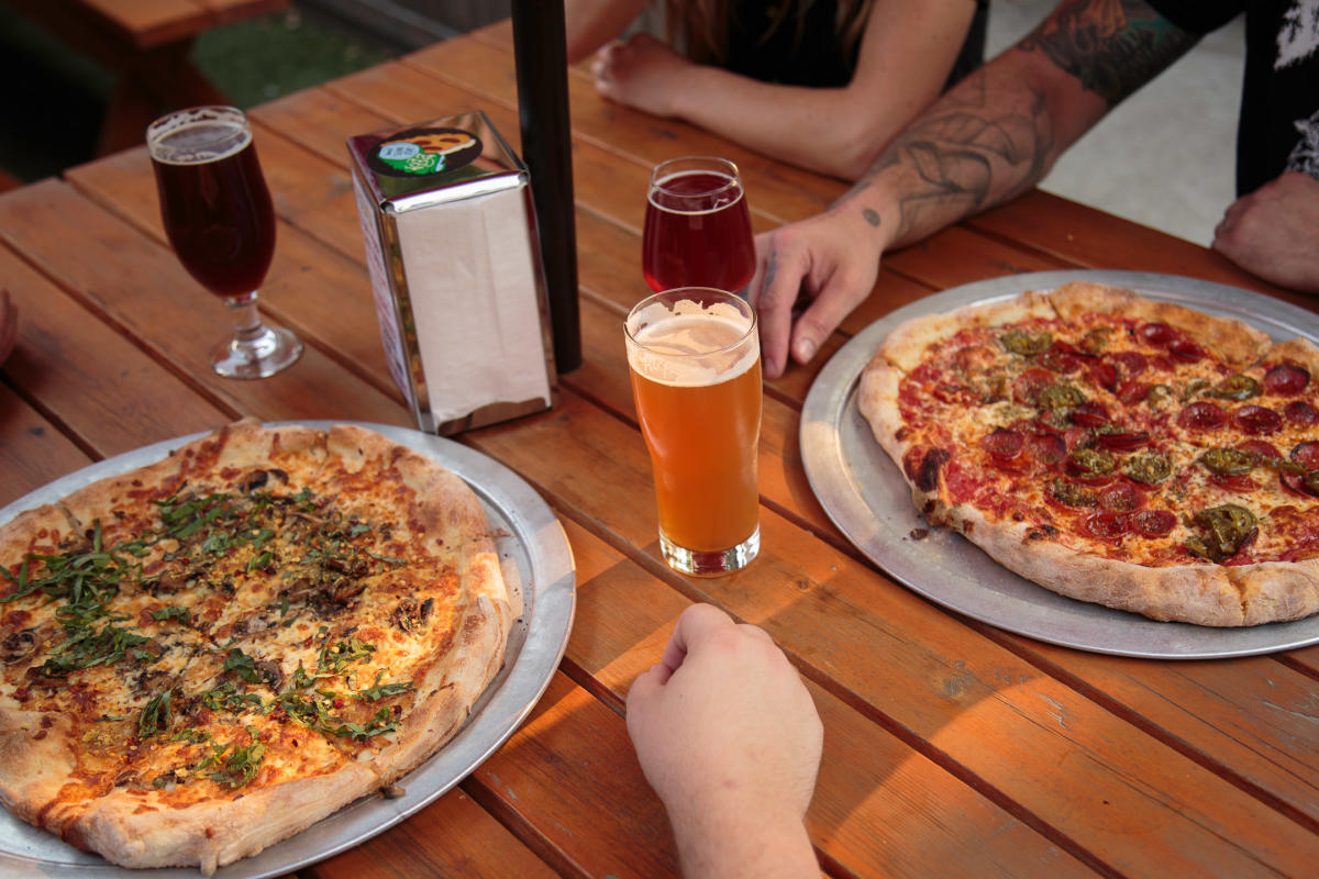 A picnic table holds two pizzas three glasses of beer at Jackknife Brewery.
