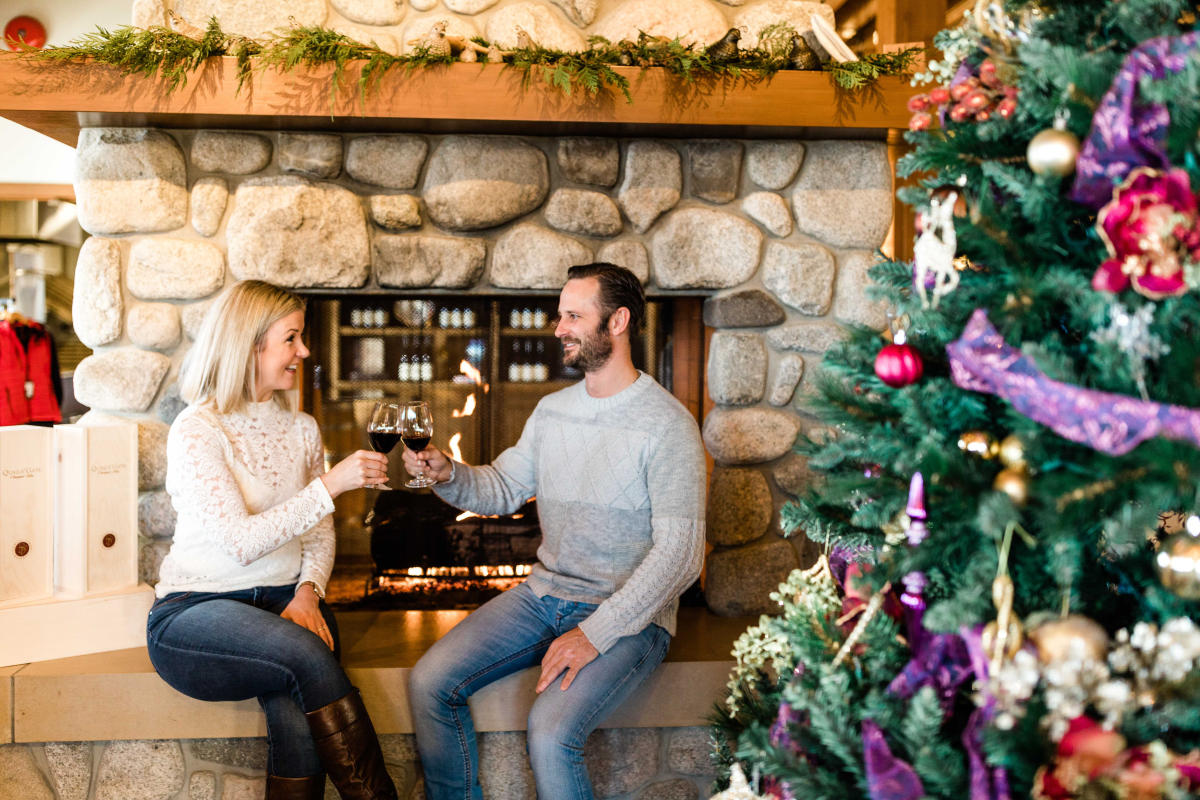 A man and woman toasting wine glasses in front of a fireplace at Quails' Gate Estate Winery 