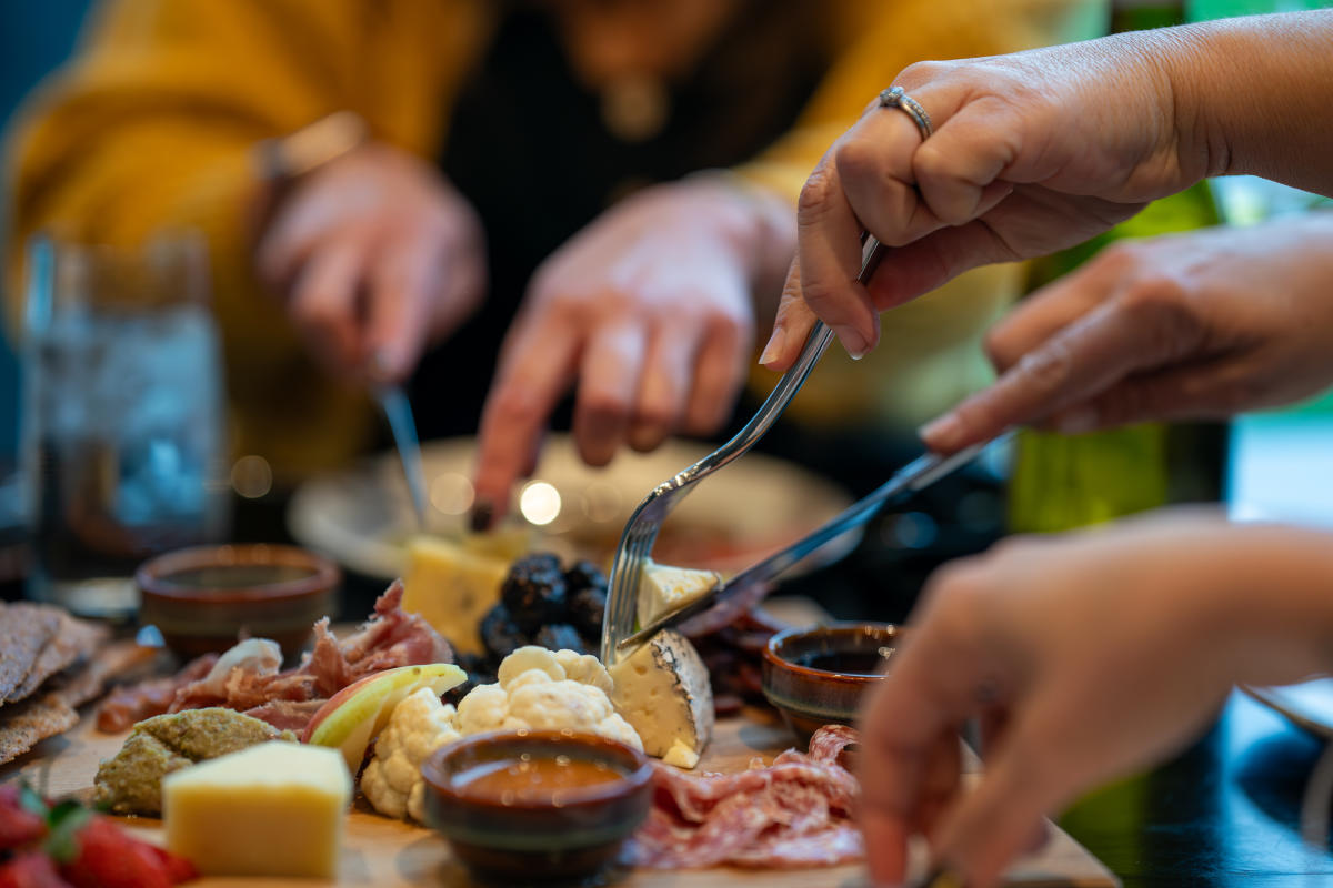 Close_Up_of_Hands_Reaching_for_Cheeses_and_Charcuterie_on_a_Shared_Tasting_Board