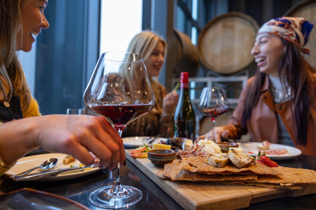 Friends_Sharing_Food_and_Red_Wine_at_a_Table_with_Wine_Barrels_in_the_Background