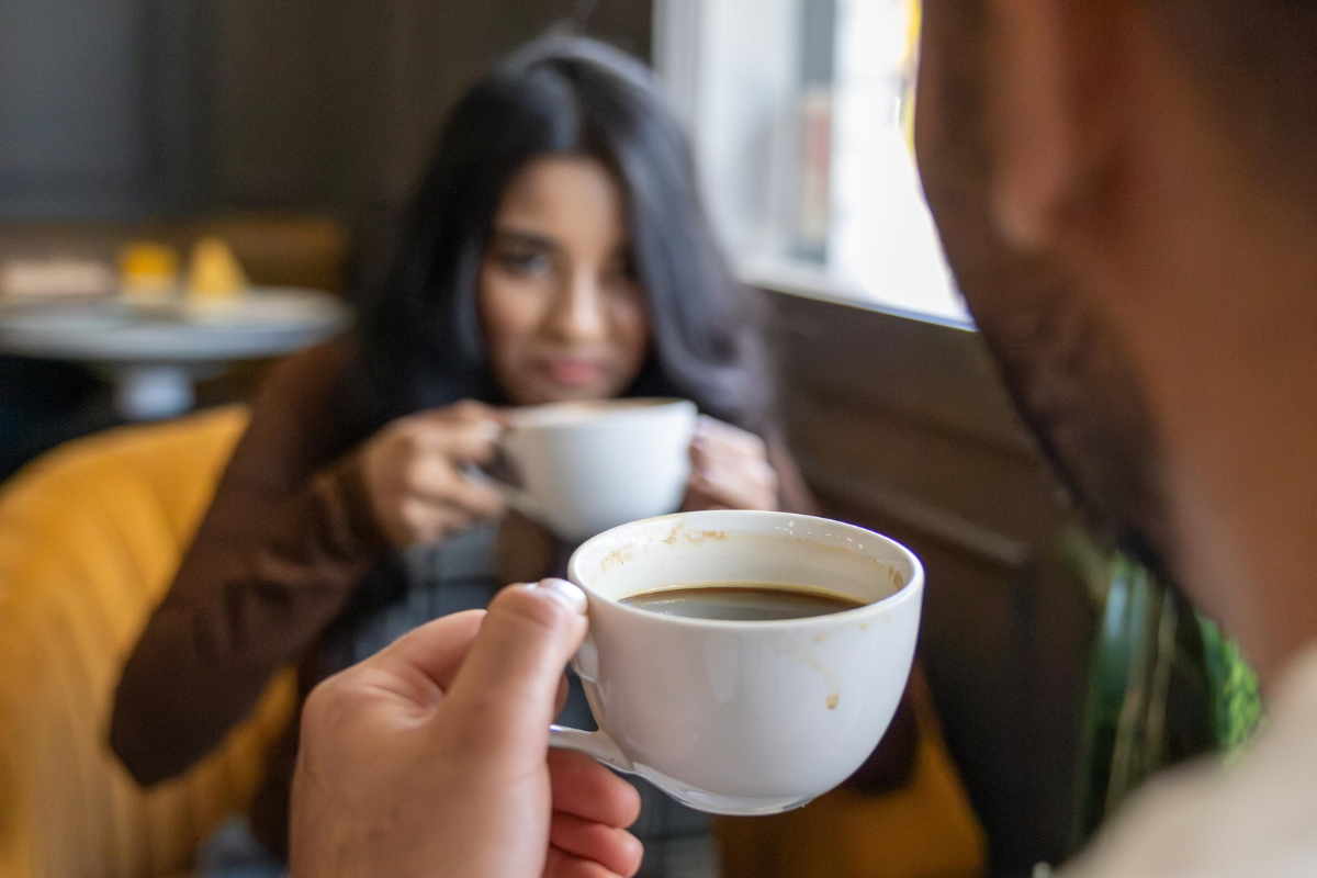 Two People Holding White Coffee Cups While Sitting Indoors at a Cafe
