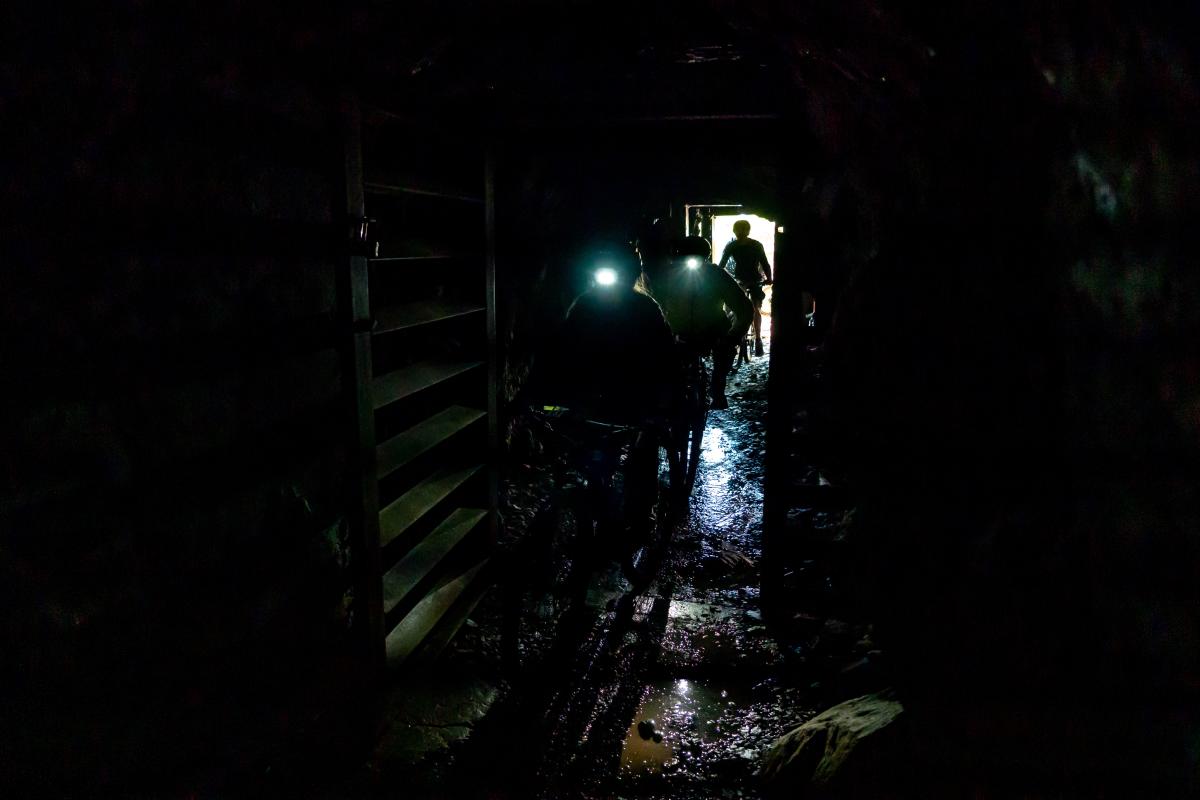 Bikers wearing headlamps bike through a mine tunnel.