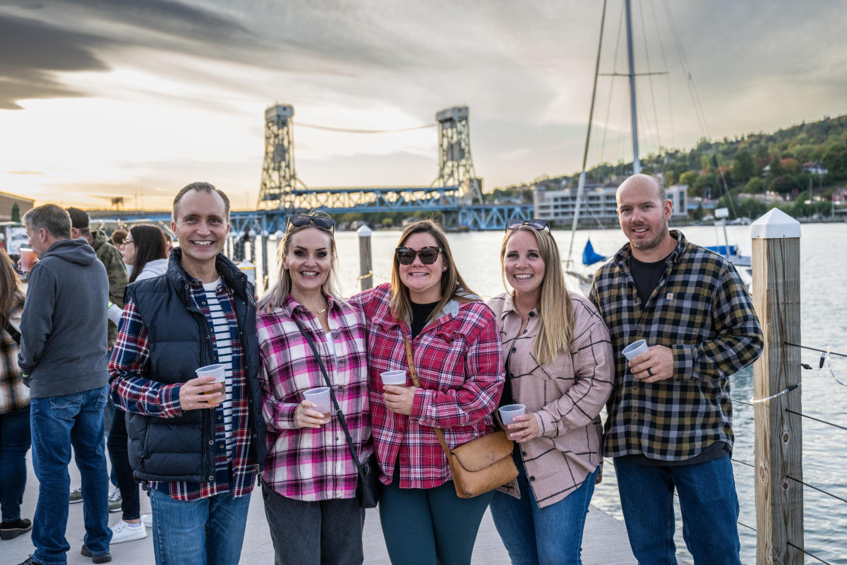 five people pose together with pints of beer smiling in fall dress