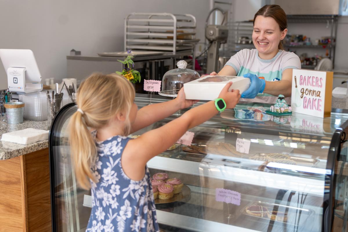a person behind a bakery counter hands off a box of pastry to a young person