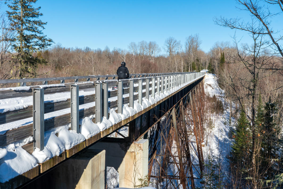 a person riding a snowmobile crosses a snowy rail trestle