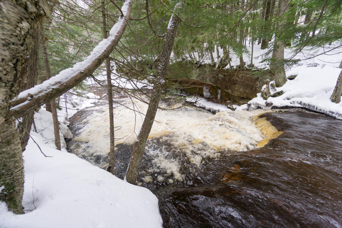 Water flows down a drop at Hogger Falls. Snow can be seen on the banks of the river.