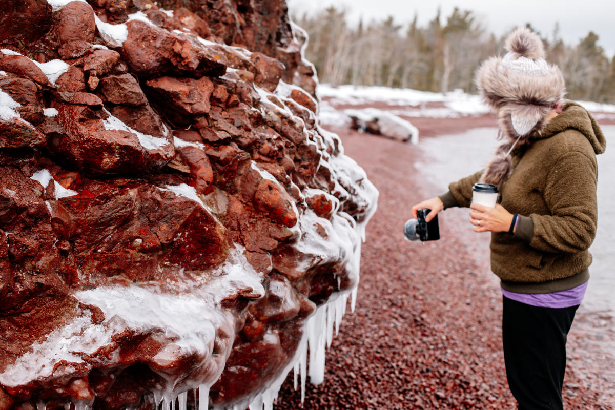 a person uses a camera to take a photo of ice formation on rocky beach