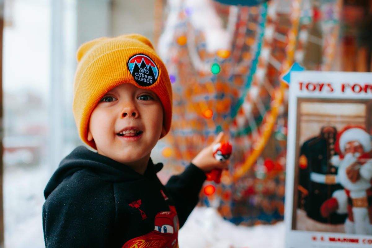 a small child in a winter beanie points to a toyshop window display